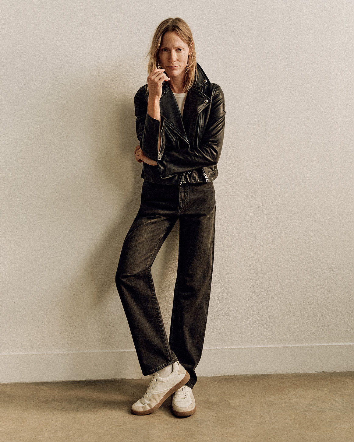 Model wearing the Sienna black leather biker jacket with dark jeans and white sneakers against a beige backdrop.
