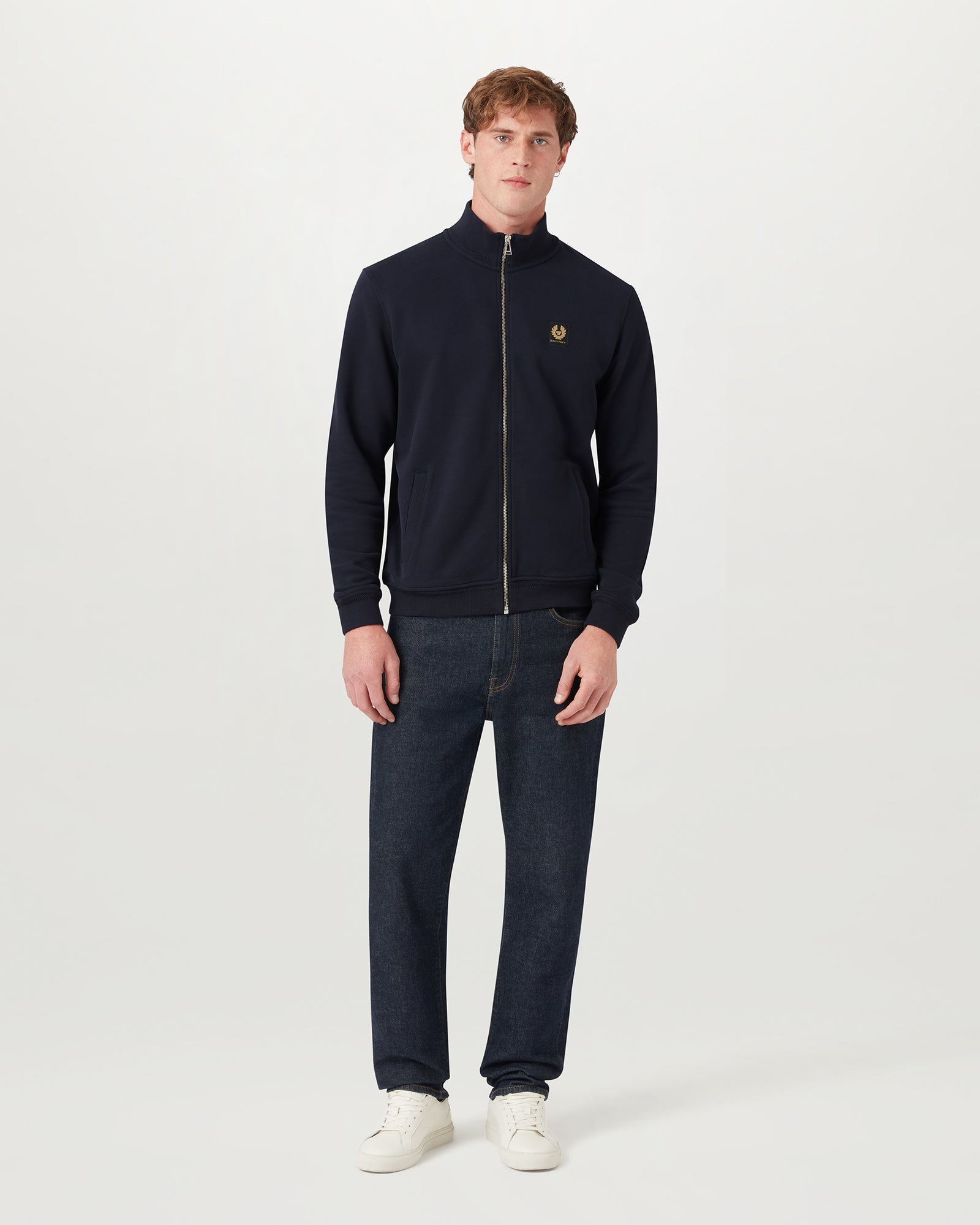 Male model wearing a navy Belstaff full zip sweatshirt with stand collar and chest logo patch