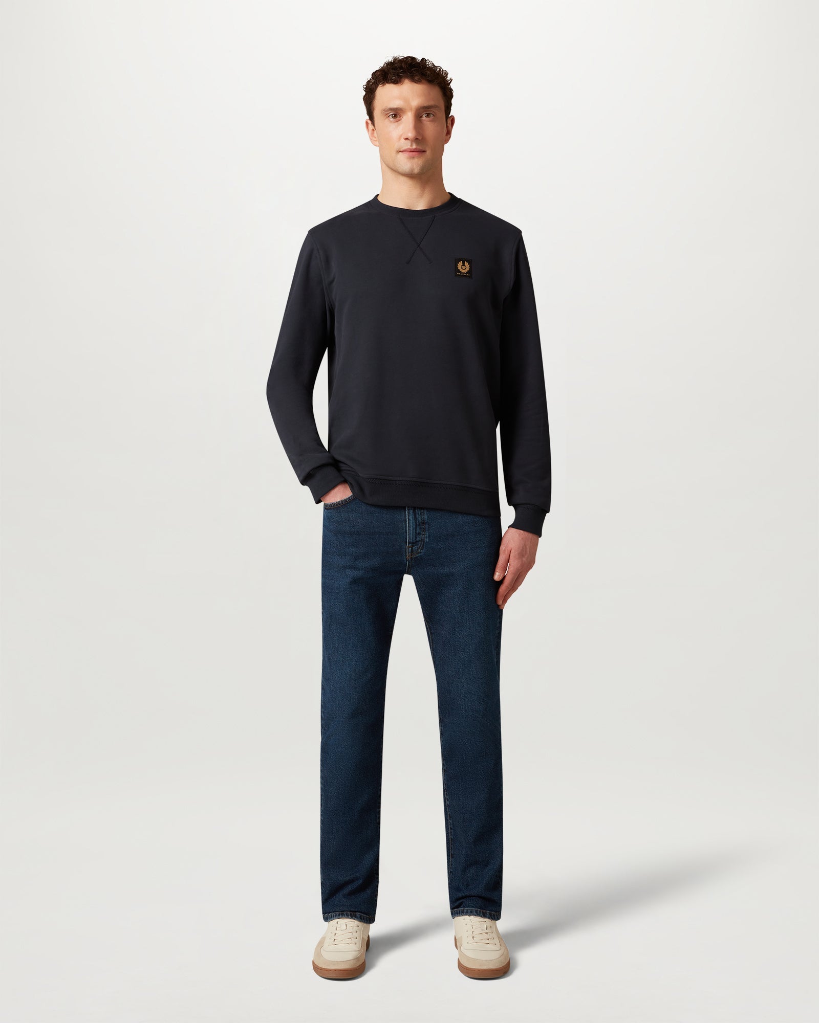 Male model wearing a dark ink Belstaff sweatshirt with a chest logo patch.