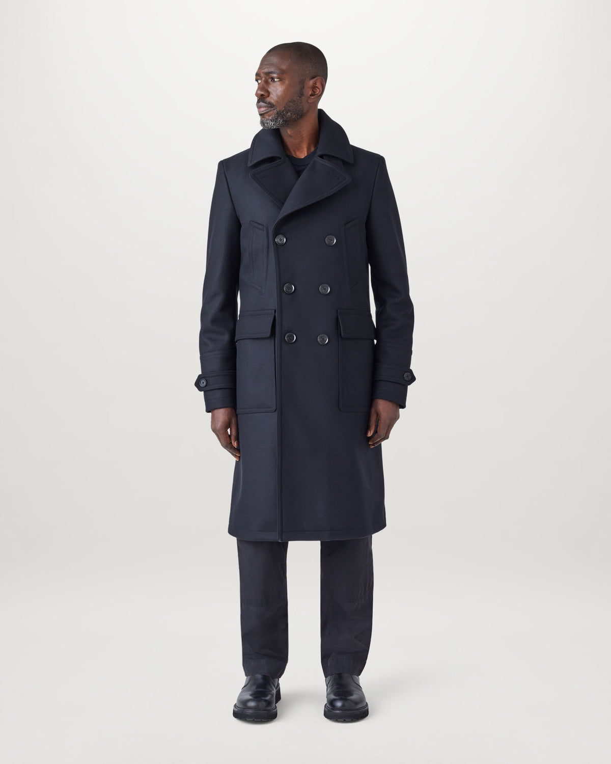 Male model wearing a navy Milford coat with a double-breasted front, epaulettes and belted waist.