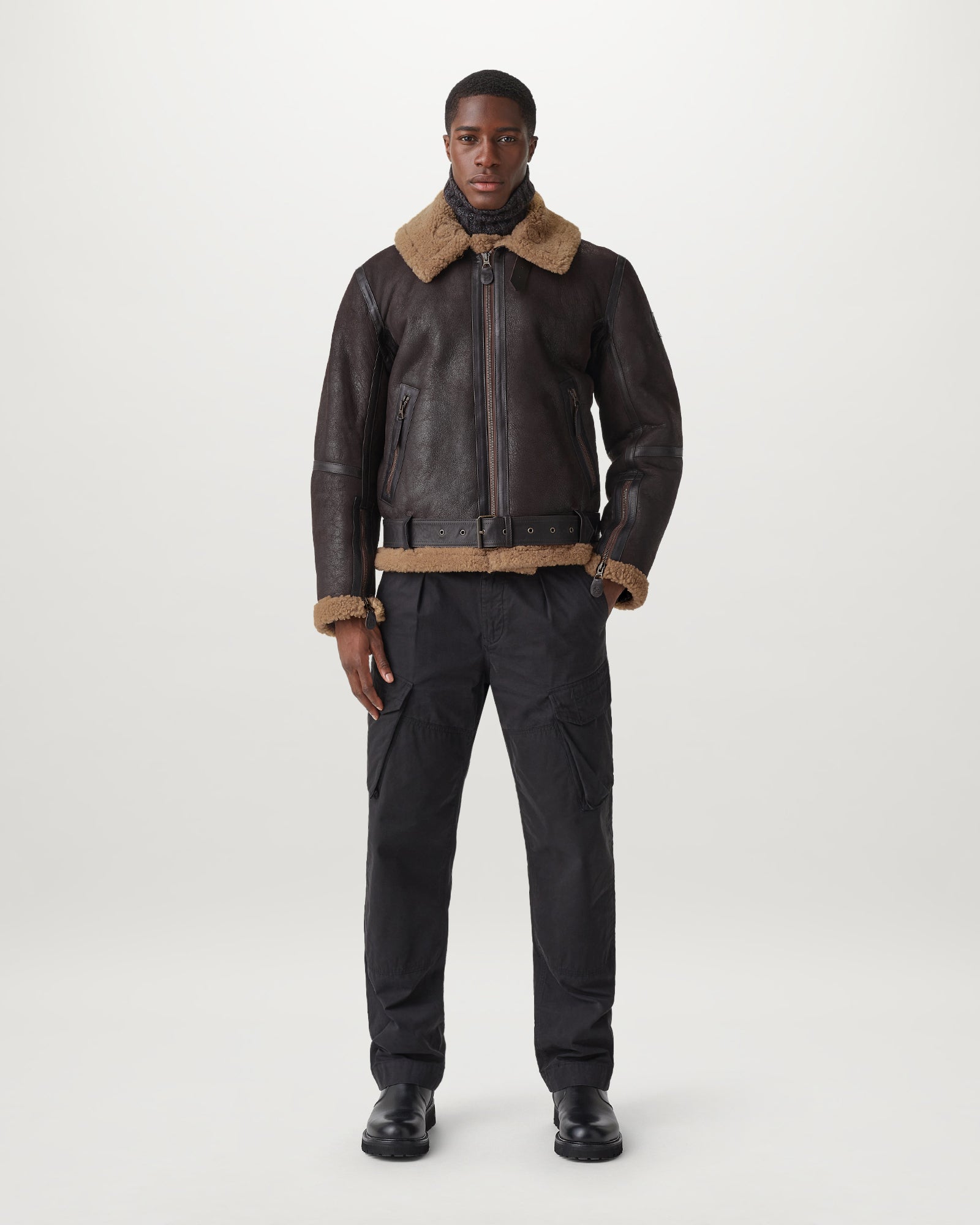 Front view of a model wearing the Wilder Jacket in dark leather with tan shearling collar and brass-tone hardware.